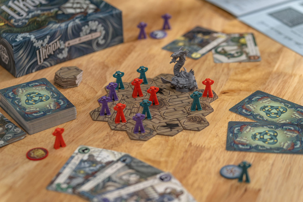 The Uk'otoa board game laid out on a table, with hexes, meeples, cards, game box, and the rulebook peeking into the screen.